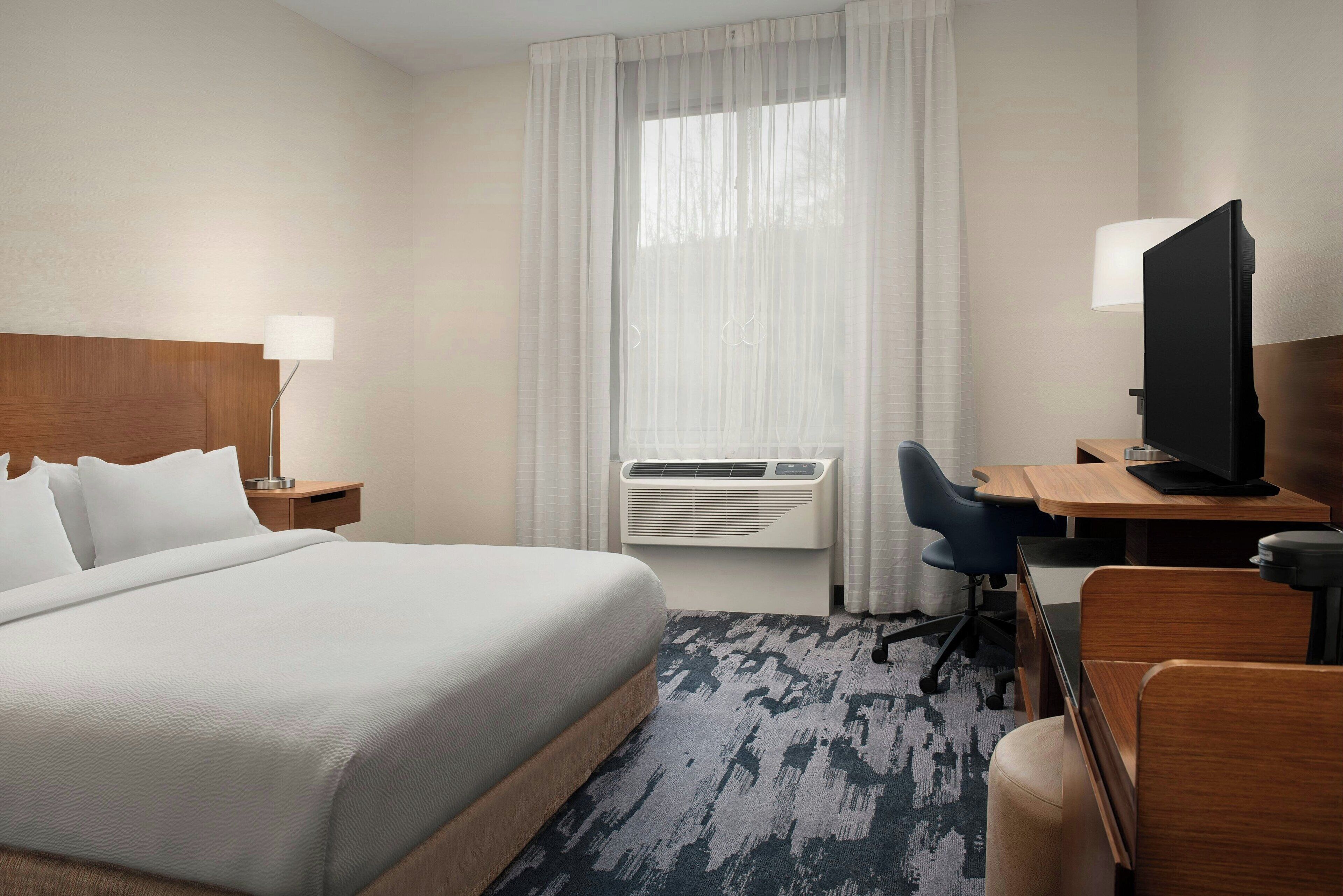 Quarto de hotel com cama, escrivaninha, cadeira, televisão e ar condicionado.