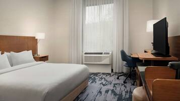 Quarto de hotel com cama, escrivaninha, cadeira, televisão e ar condicionado.