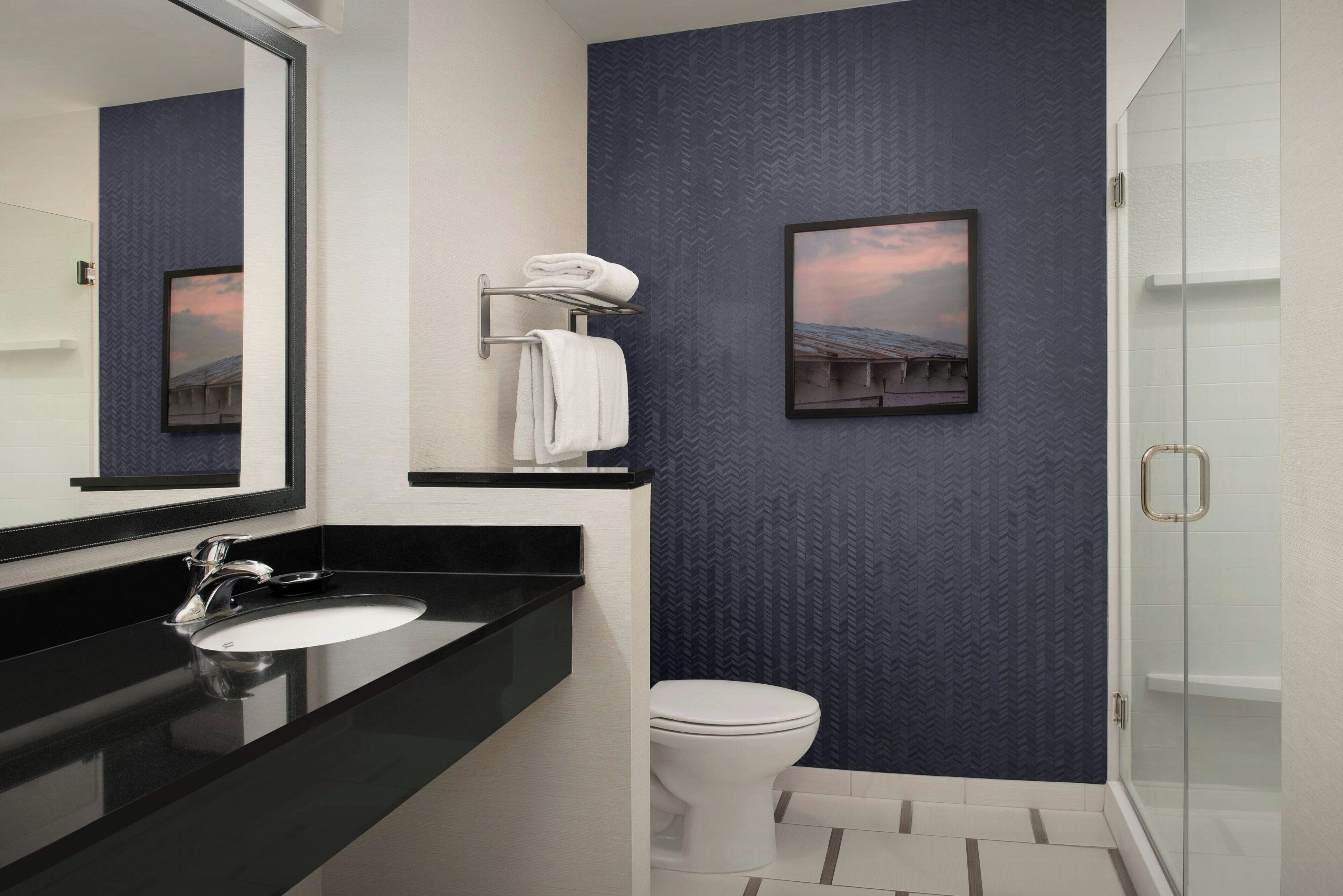 Un baño moderno con encimera negra, lavamanos blanco y cabina de ducha de vidrio.