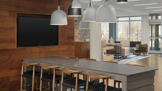 Une salle de conférence moderne, dotée d’une grande table, de chaises en bois et d’un système d’éclairage suspendu.