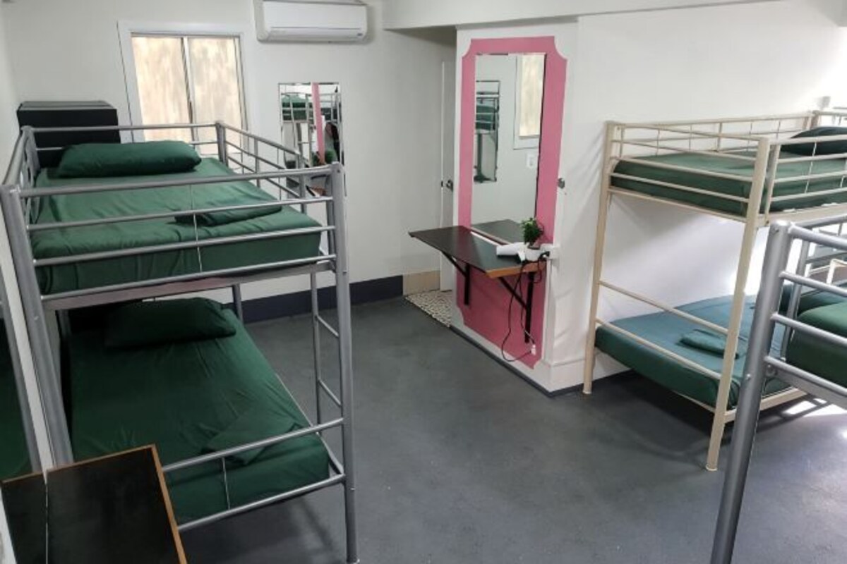 A dormitory room with bunk beds, a desk, and a mirror.
