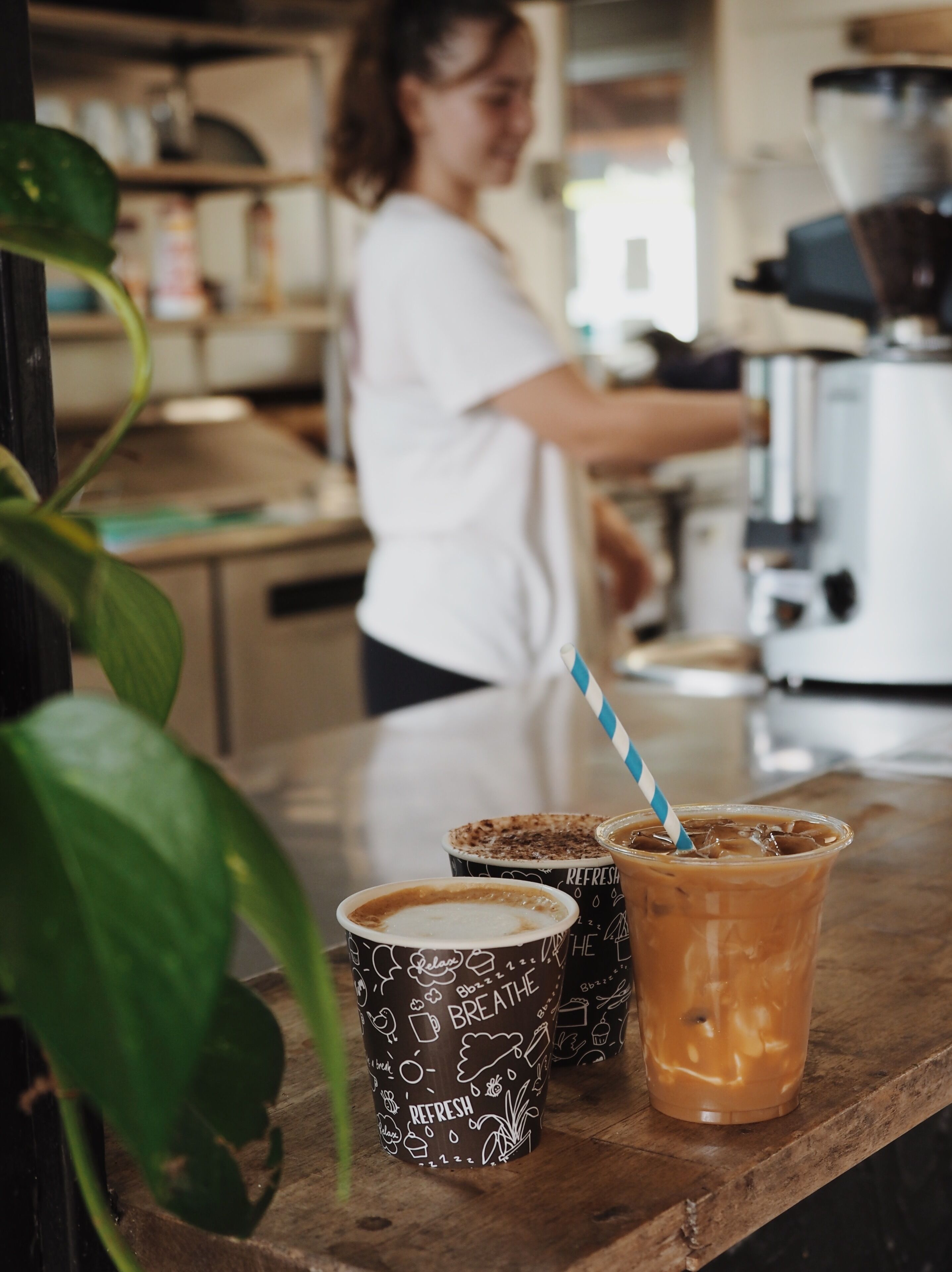A barista preparing drinks behind a counter with two cups of coffee and a large iced coffee.