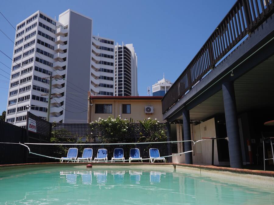 A swimming pool with lounge chairs, a building with multiple floors, and an overpass in the background.