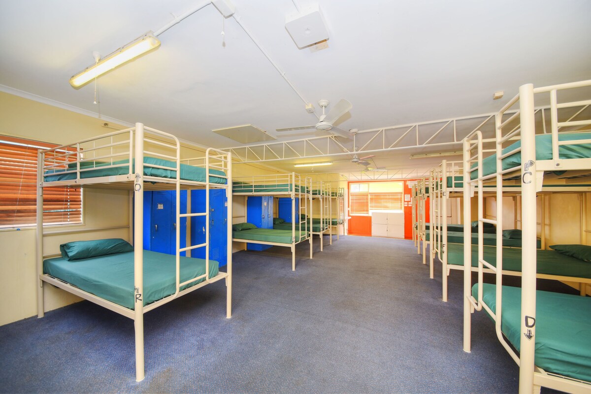 A dormitory with bunk beds, a ceiling fan, and a window with blinds.