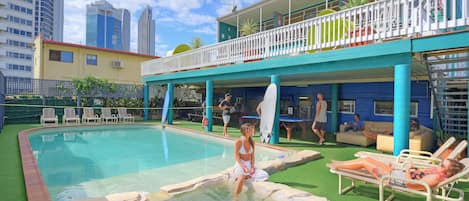 A pool area with lounge chairs and a building with a balcony.