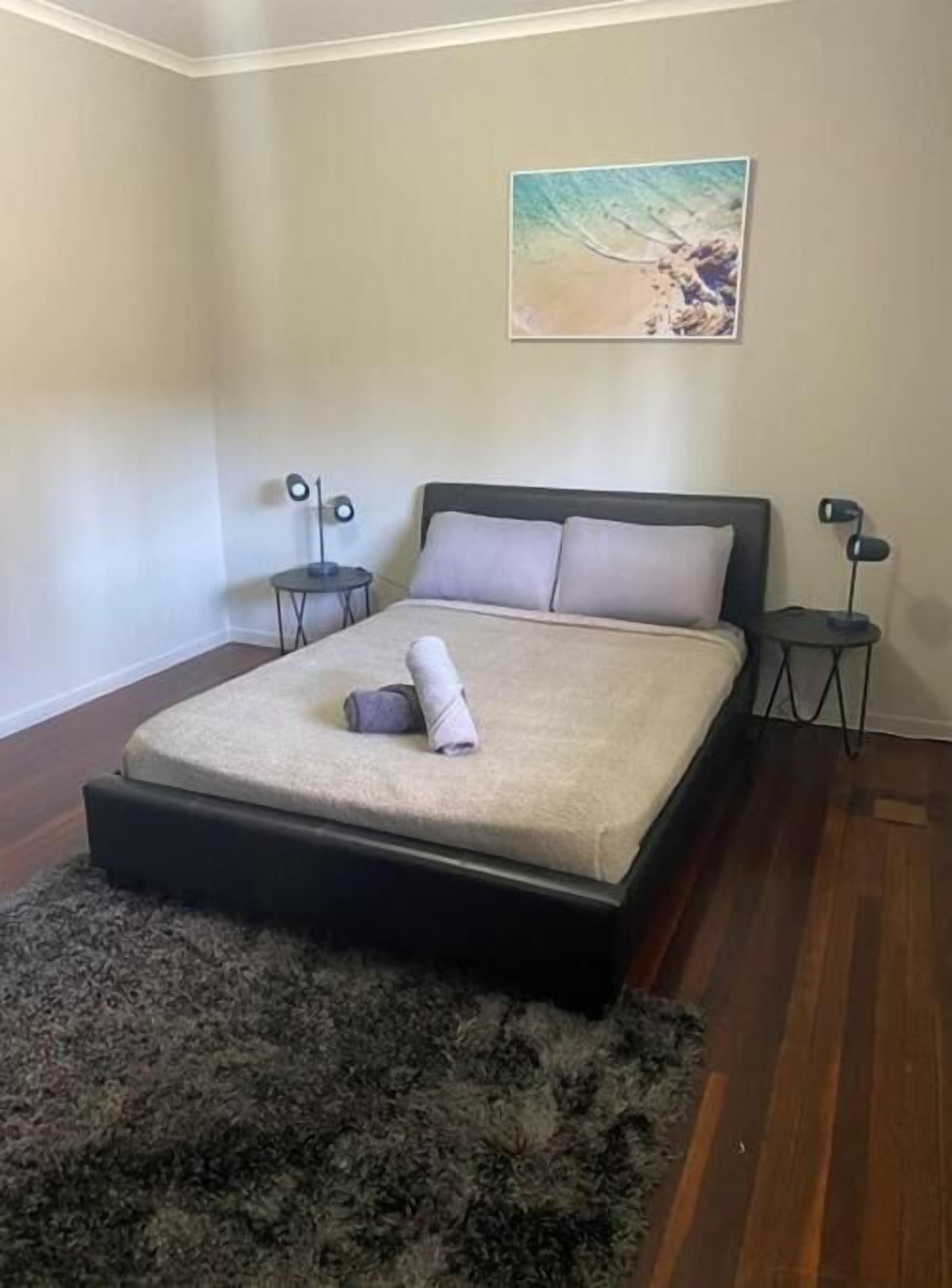 A bedroom with a bed, a rug, a painting, and two bedside tables.