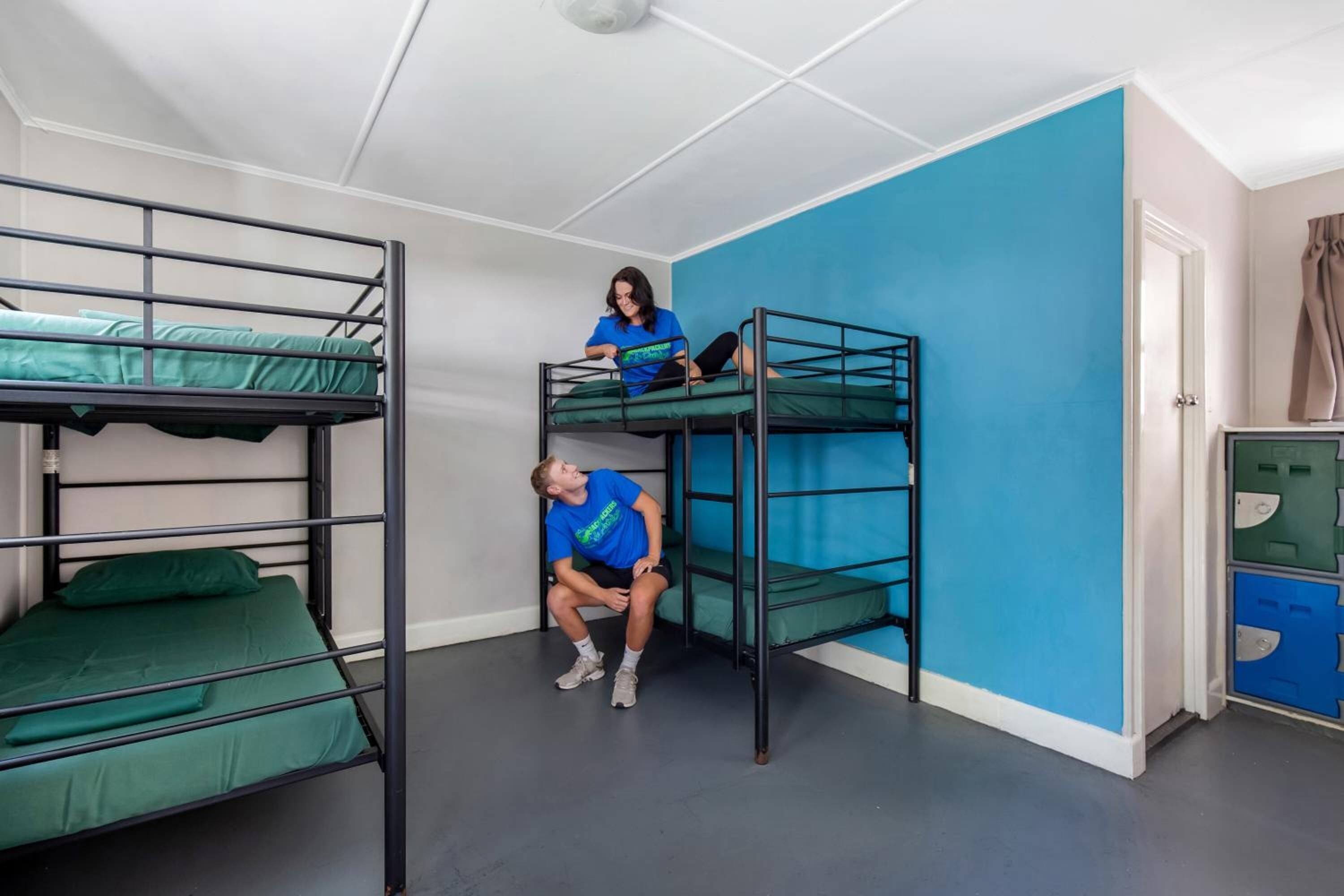 Ein Schlafsaalzimmer mit Etagenbetten, einer blauen Wand und einer Tür mit Vorhang.