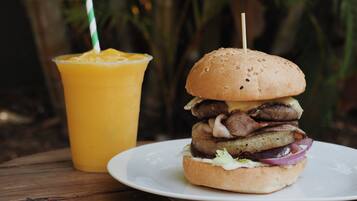 A burger with a toothpick on a white plate, a yellow drink with a striped straw, and a wooden table.