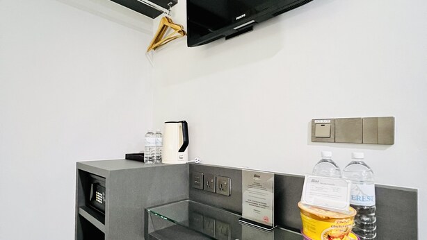 Une salle de bain moderne avec un meuble-lavabo gris, un téléviseur à écran plat noir fixé au mur, une étagère en verre contenant des articles de toilette et une poubelle.