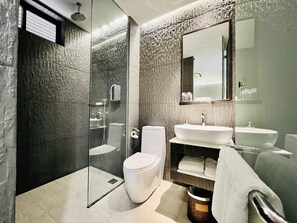 Un baño moderno con ducha envuelta en vidrio, inodoro blanco, lavamanos y espejo.