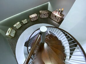 Una escalera de caracol con barandilla, escalones alfombrados y cajas decorativas con velas en el rellano.
