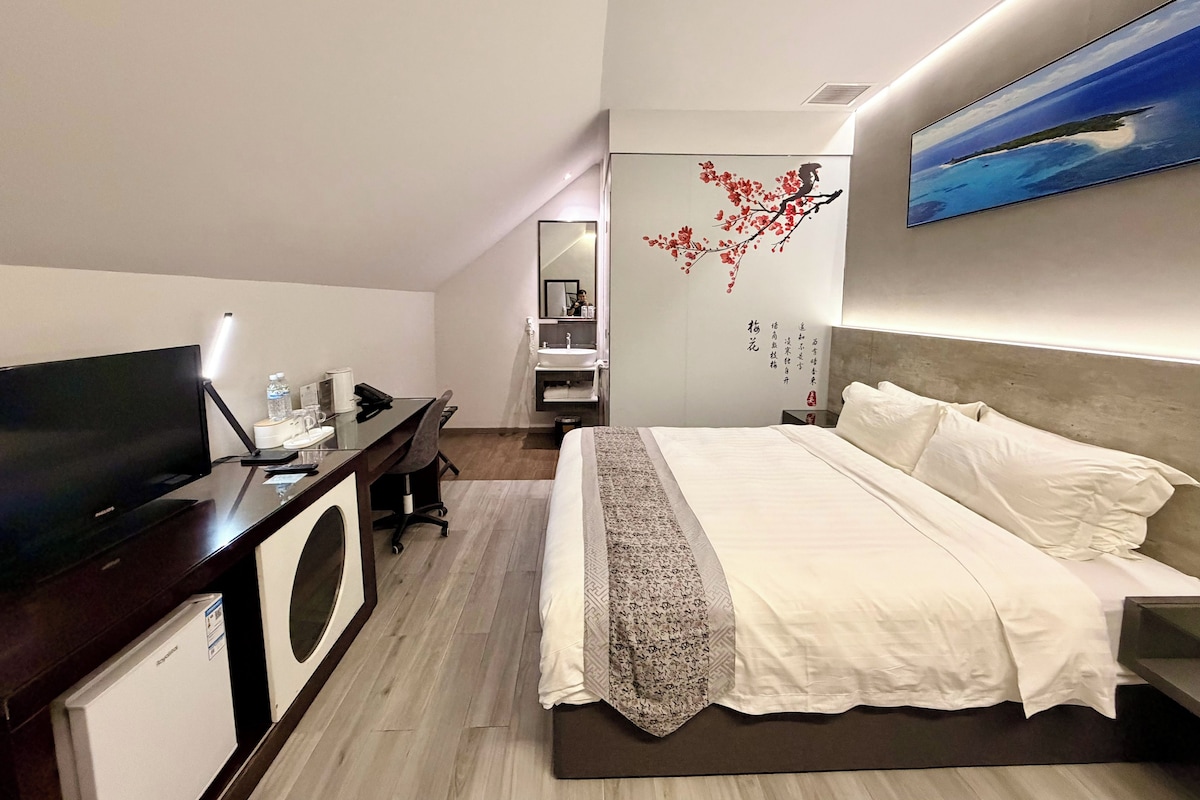 A modern hotel room with a bed, a desk with a computer, a flat-screen TV, and a bathroom with a sink and mirror.