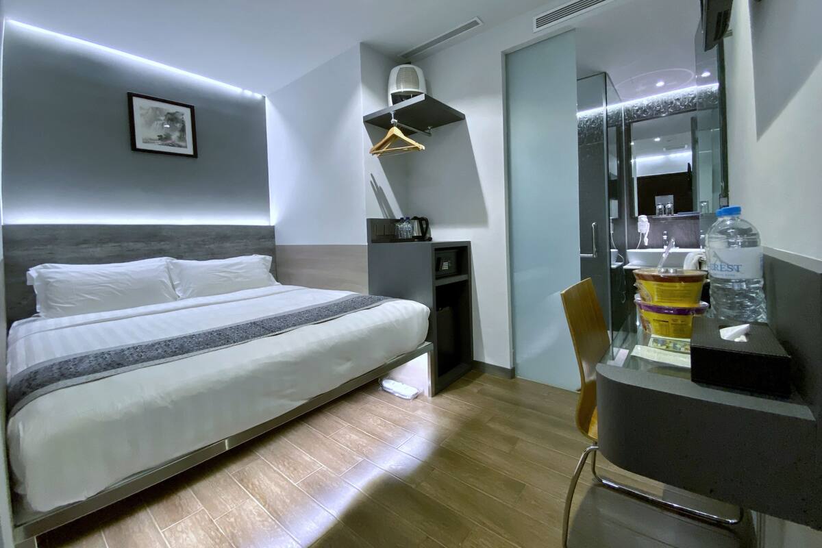 Une chambre d’hôtel moderne avec un lit bien fait, un bureau avec une chaise, un grand miroir et un distributeur d’eau.