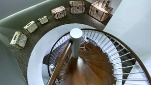 Una escalera de caracol con barandilla, escalones alfombrados y cajas decorativas con velas en el rellano.