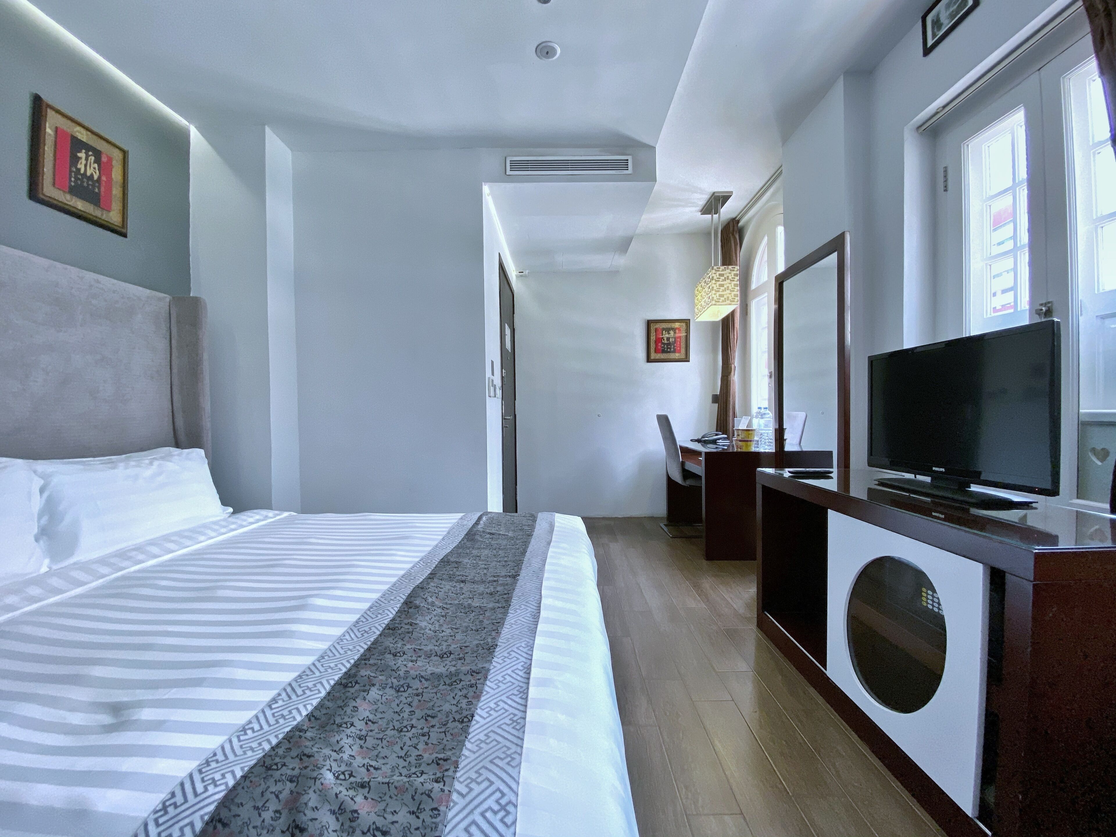 A hotel room with a bed, a desk, a television, and a window.