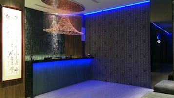 Un spa moderno con pared de piedra, panel de madera, mostrador de recepción iluminado en azul y una obra de arte grande enmarcada.