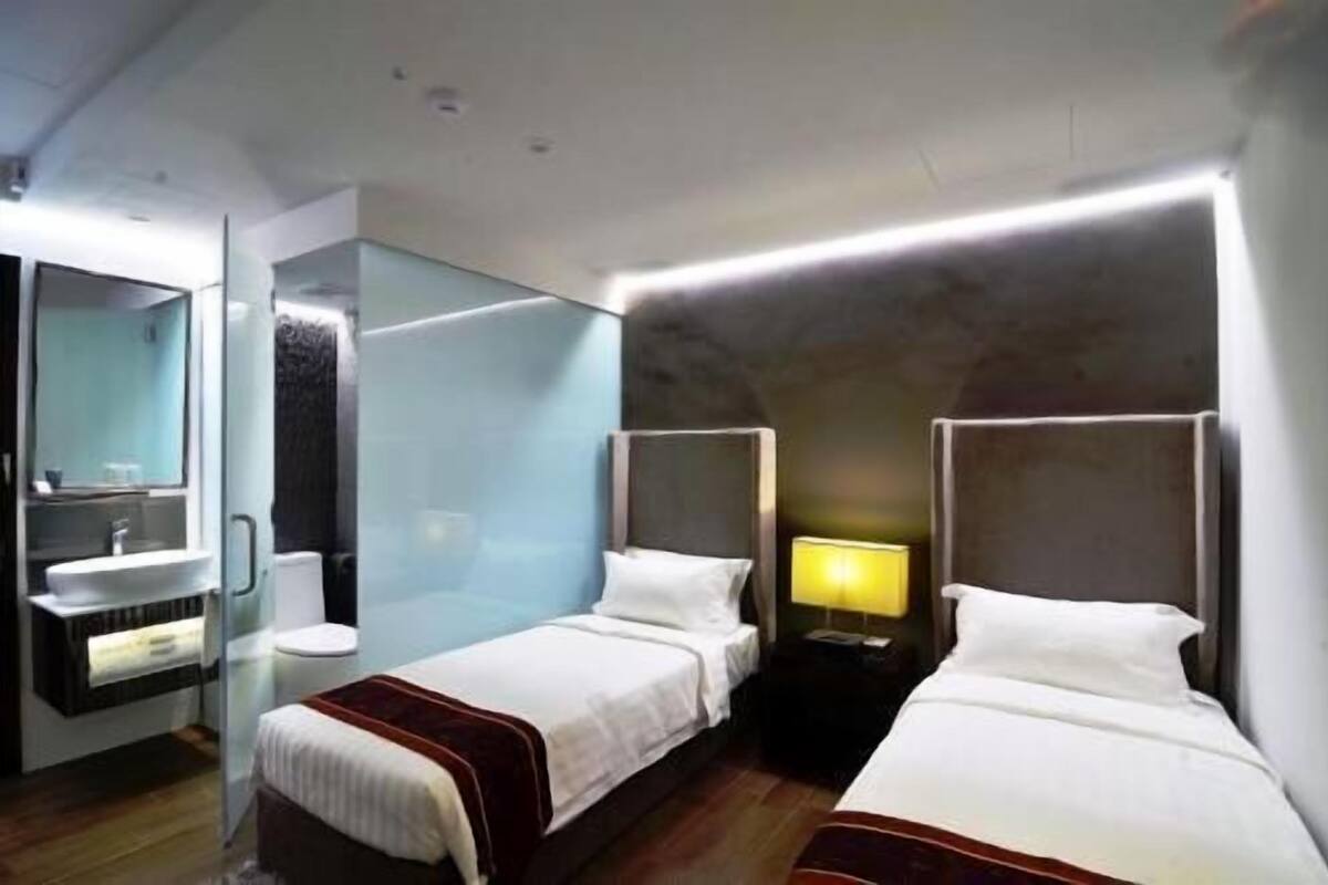 Une chambre d’hôtel avec deux lits, une salle de bain et une table de chevet avec une lampe.