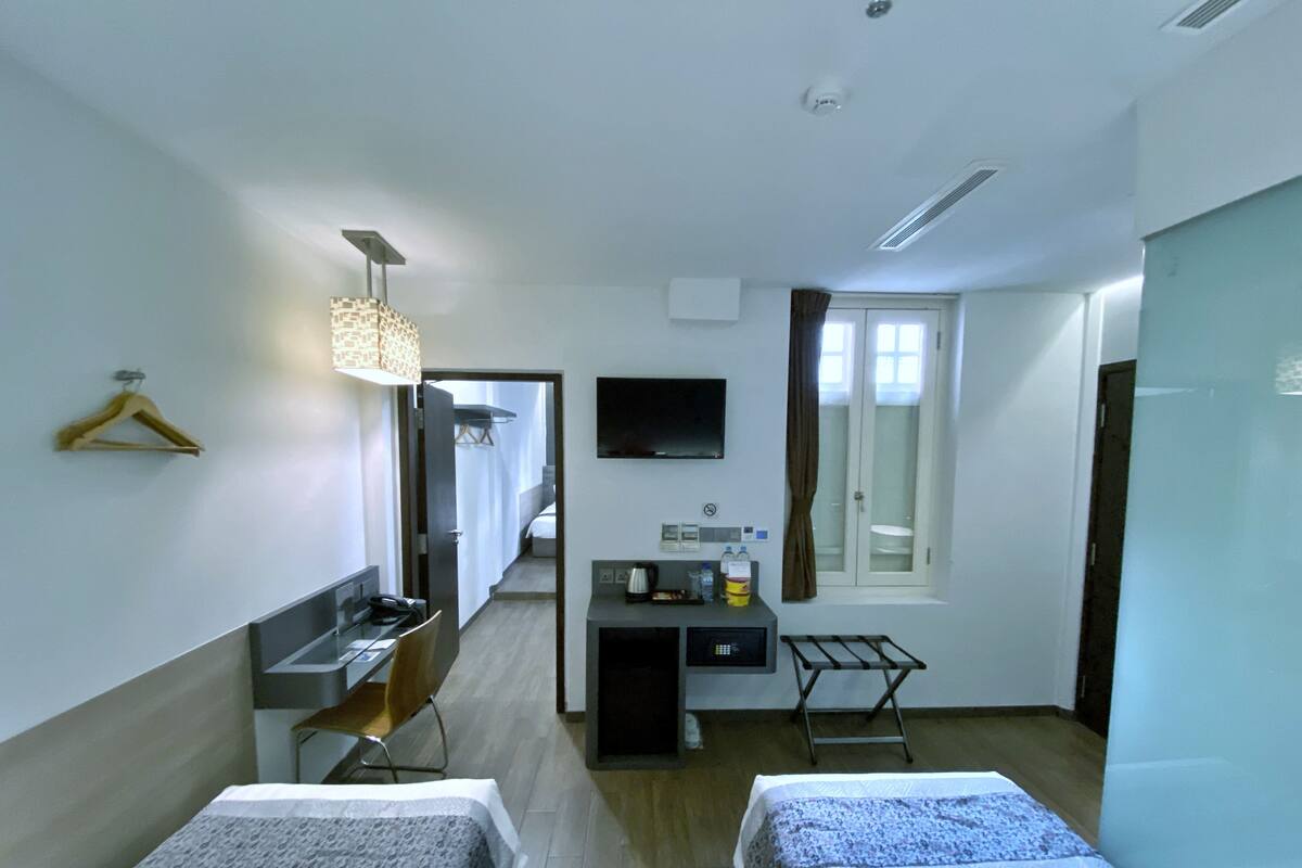 Une chambre d’hôtel avec deux lits, un bureau, une chaise, une télévision, un miroir, une fenêtre et un porte-vêtements.