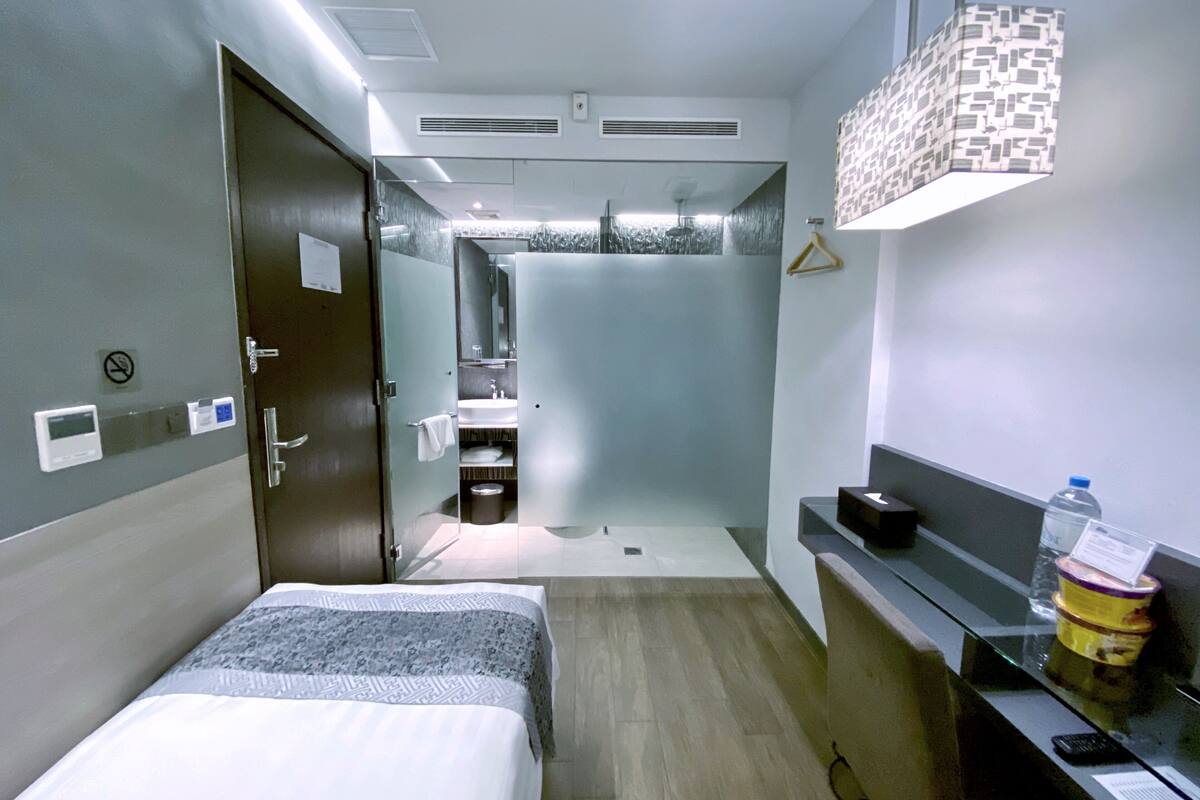 Une chambre d’hôtel avec un lit, une salle de bain avec une douche, un lavabo et un miroir. On y trouve un porte-serviettes et une bouteille d’eau sur le comptoir.