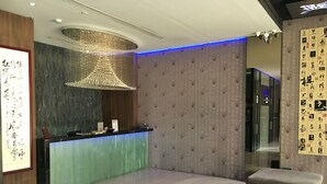 Un área de recepción de diseño moderno, con mostrador de recepción, una lámpara colgante decorativa y una zona de estar con sillones acolchados.