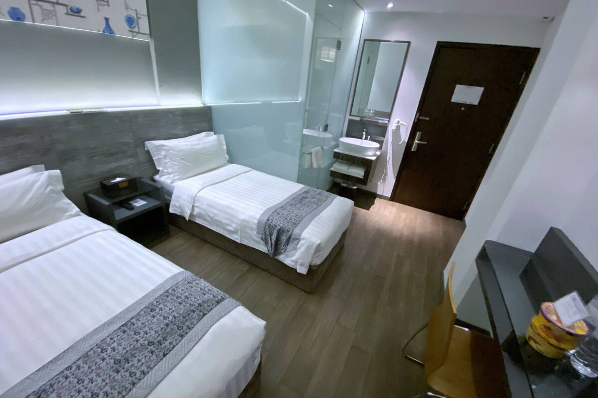 Une chambre d’hôtel avec deux lits, une table de chevet, une télévision et une salle de bain avec un miroir, ainsi qu’une porte.