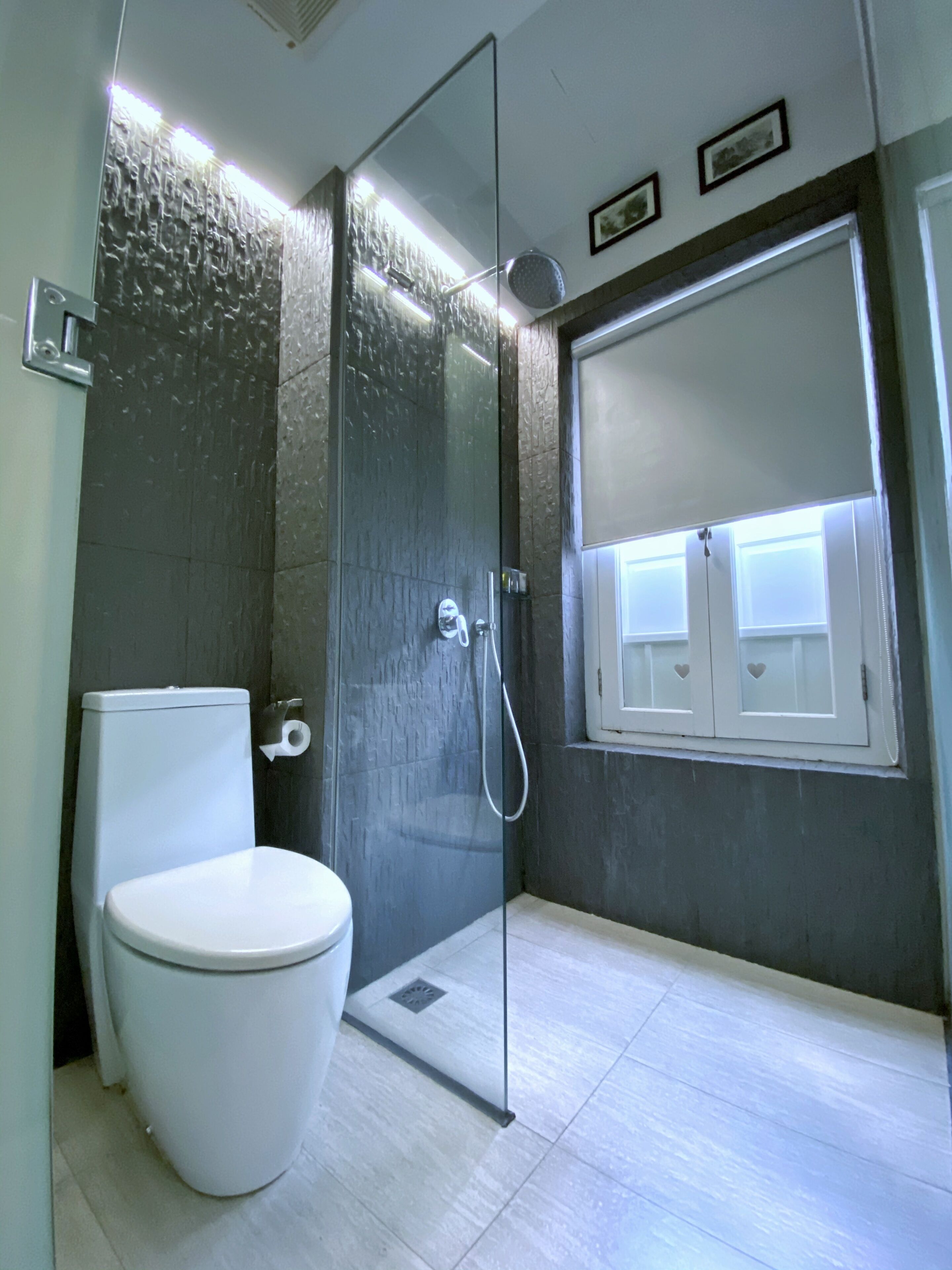 Un baño moderno con cabina de ducha de vidrio, un inodoro y una ventana con recortados en forma de corazón.