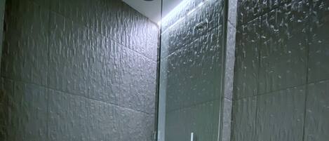 A modern bathroom with a glass-enclosed shower, a white toilet, and a textured wall.