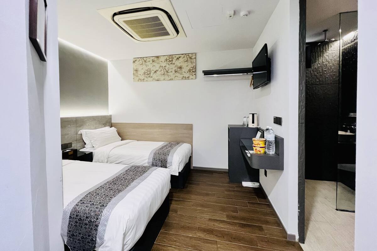 Une chambre d’hôtel avec deux lits, une petite kitchenette, un téléviseur fixé au mur et une bouche d’aération au plafond.