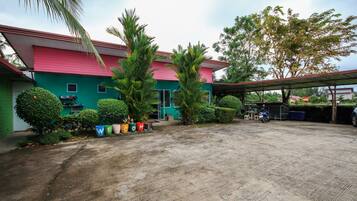 A spacious outdoor area with a concrete floor, surrounded by greenery and a colorful building with a red roof.