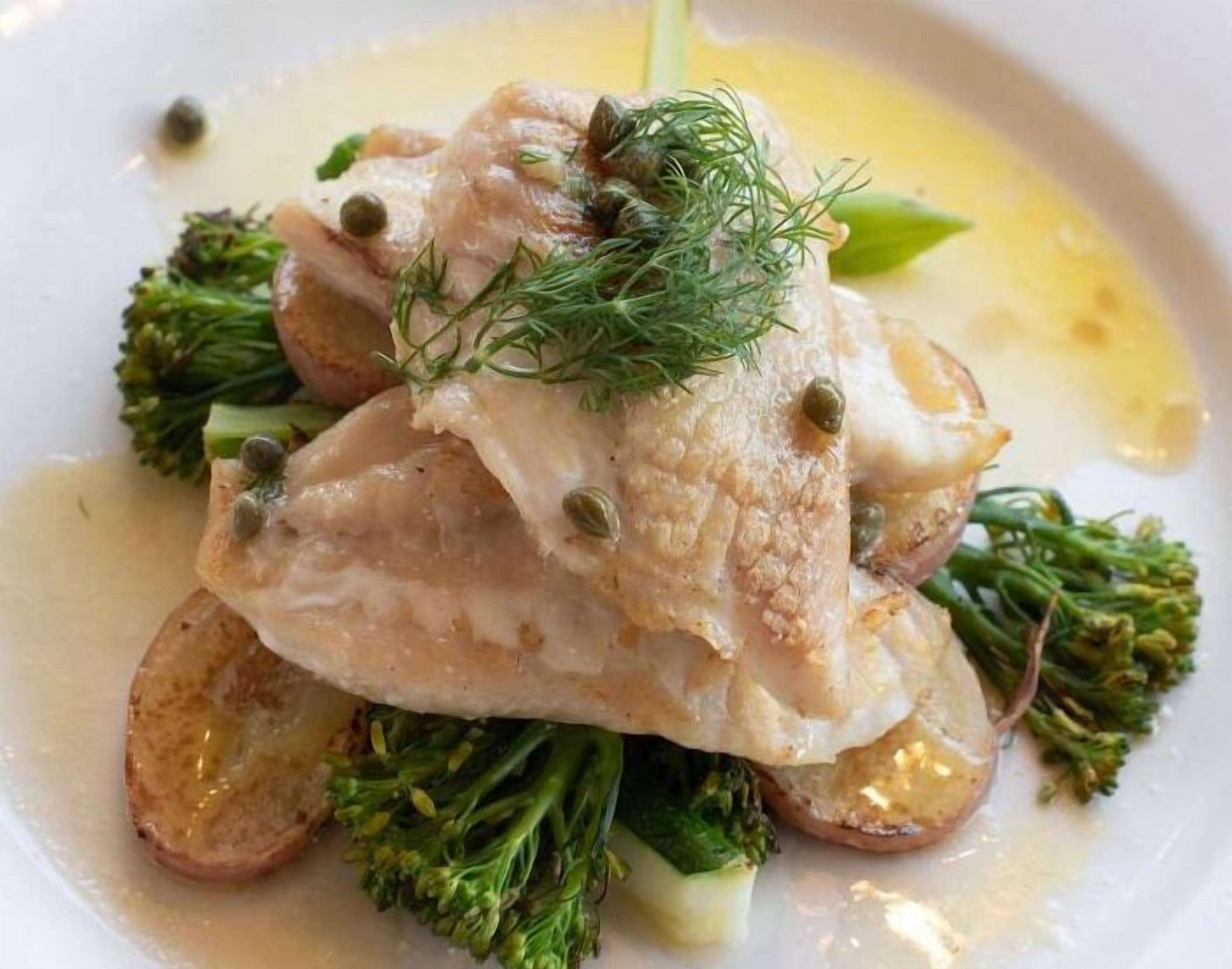 Un plato con pescado, brócoli y alcaparras.