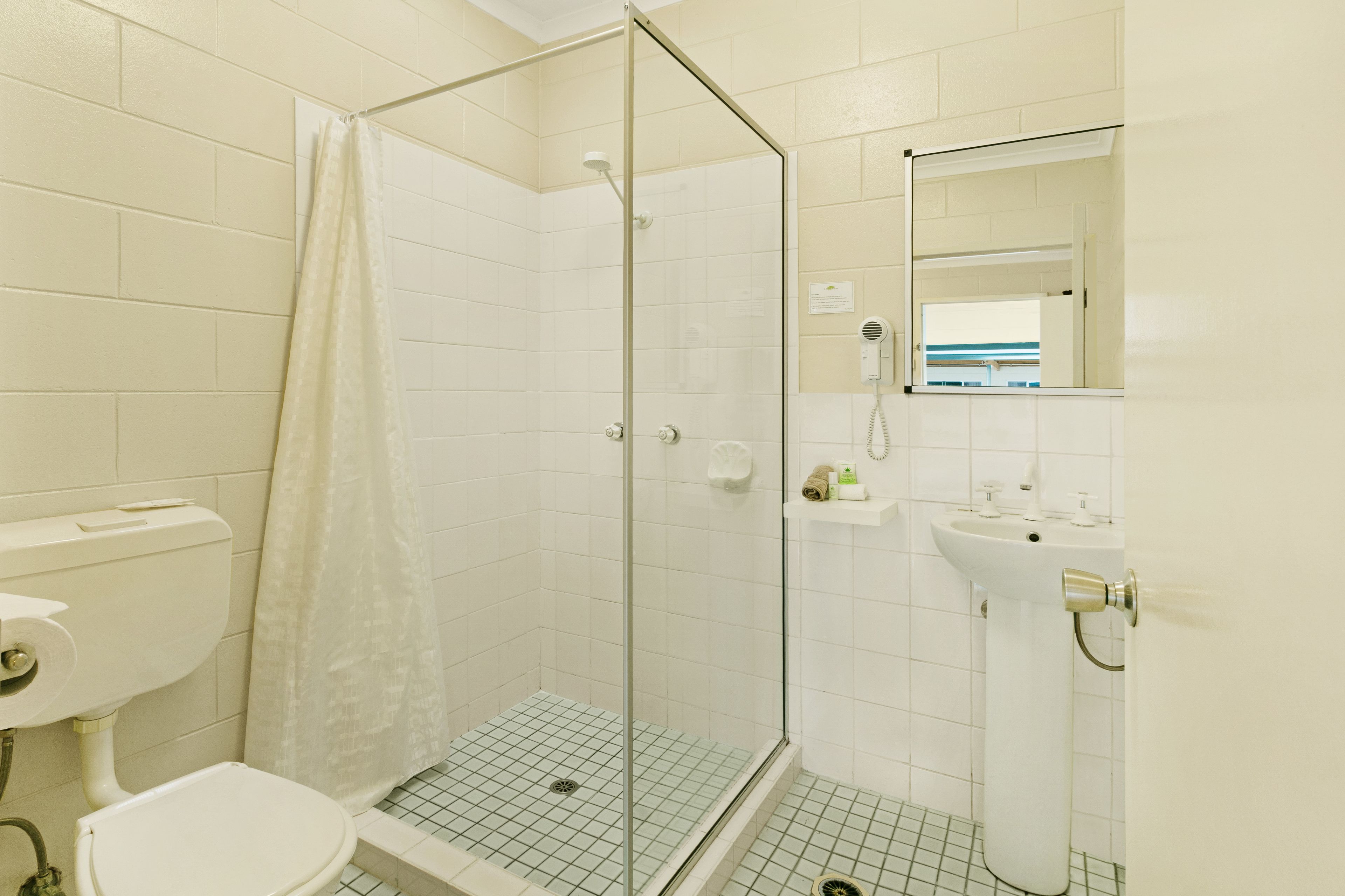 A bathroom with a glass-enclosed shower, a toilet, and a sink with a mirror above it.
