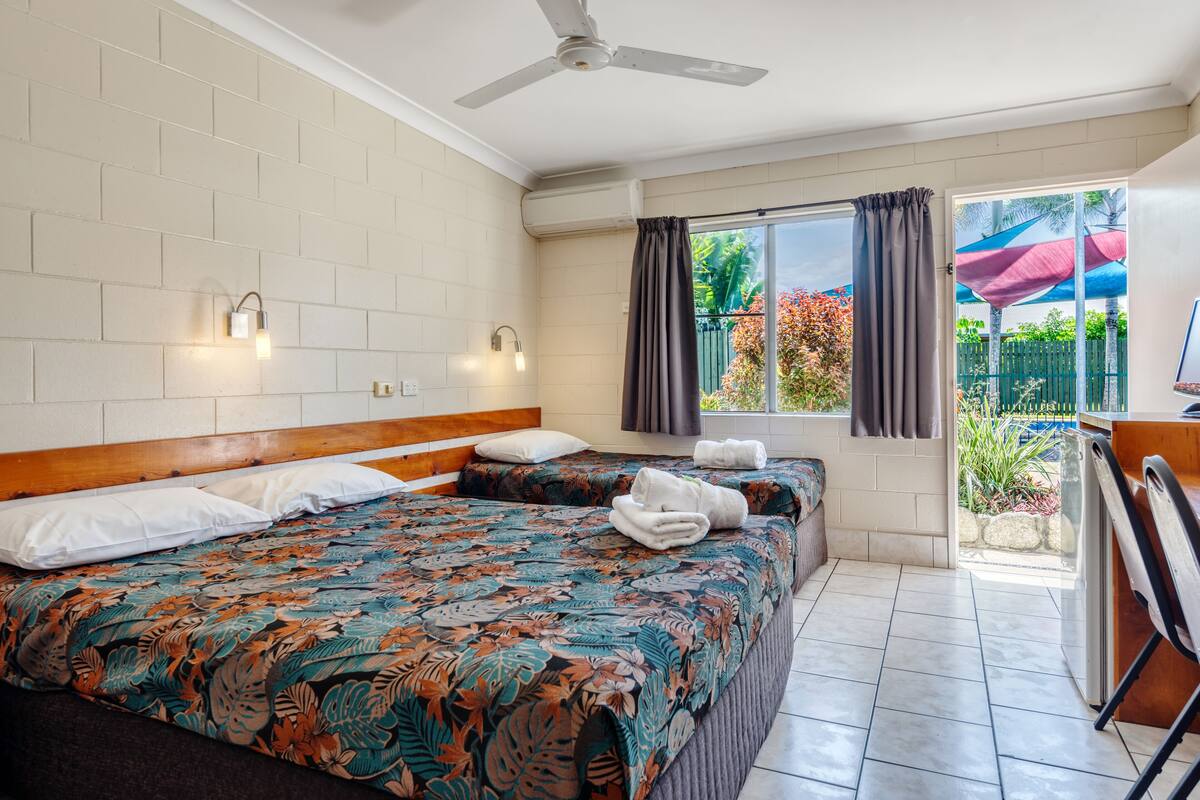 A hotel room with a large bed, a ceiling fan, a window with curtains, and a view of the outside.