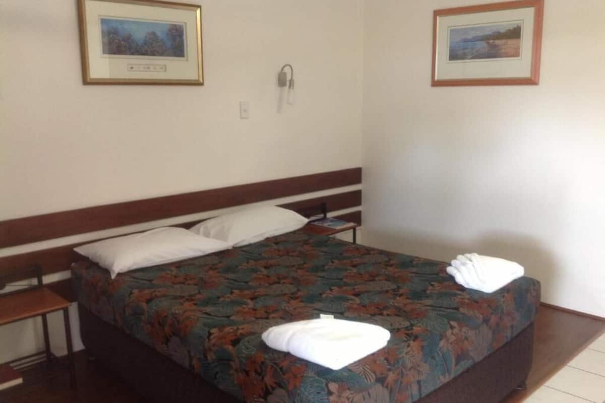 A double bed with floral bedding, two pillows, and a bedside table with a lamp.
