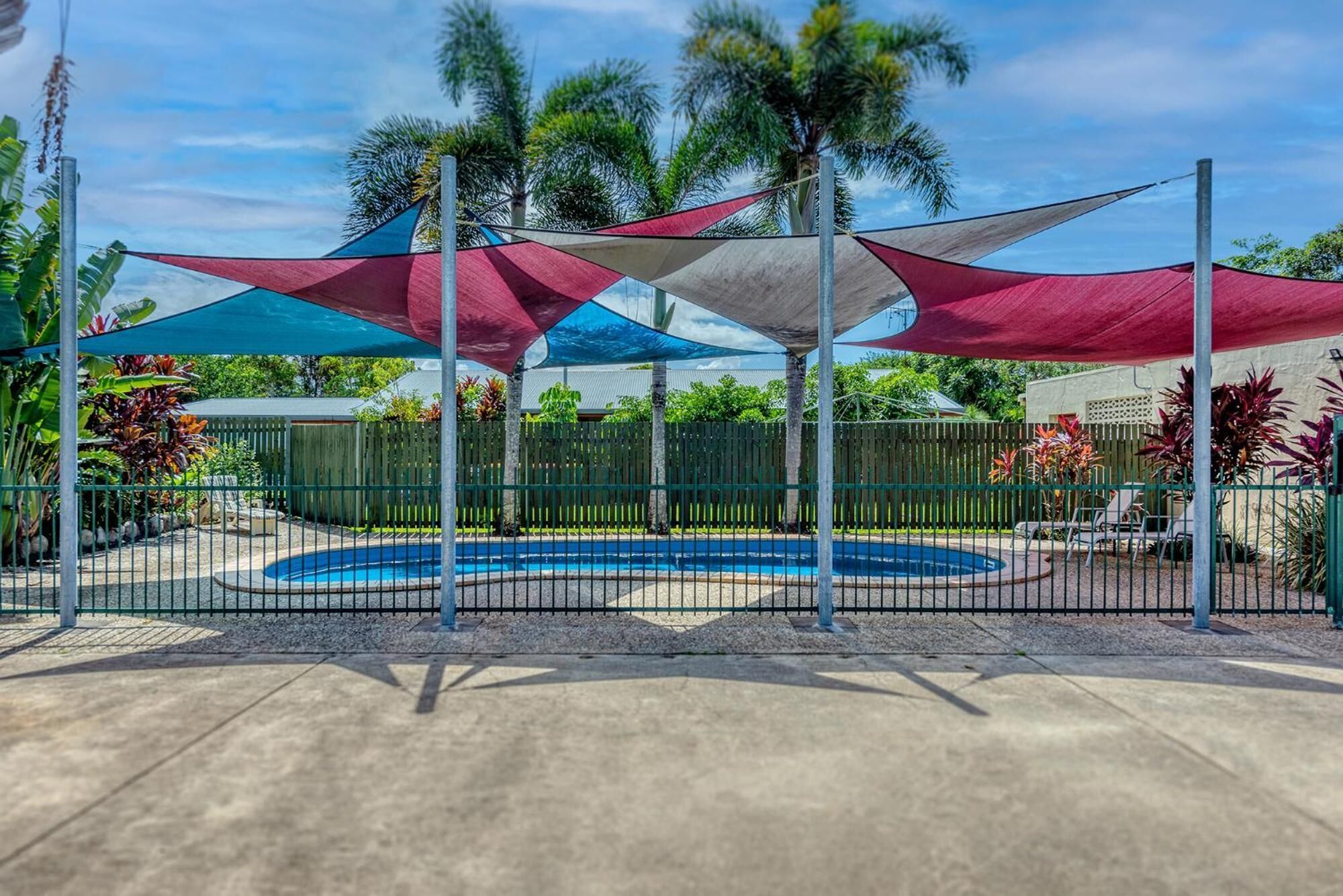 A pool area with a circular pool, surrounded by a metal fence, and shaded by multiple colorful canopies.