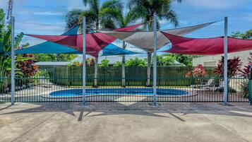 A pool area with a circular pool, surrounded by a metal fence, and shaded by multiple colorful canopies.