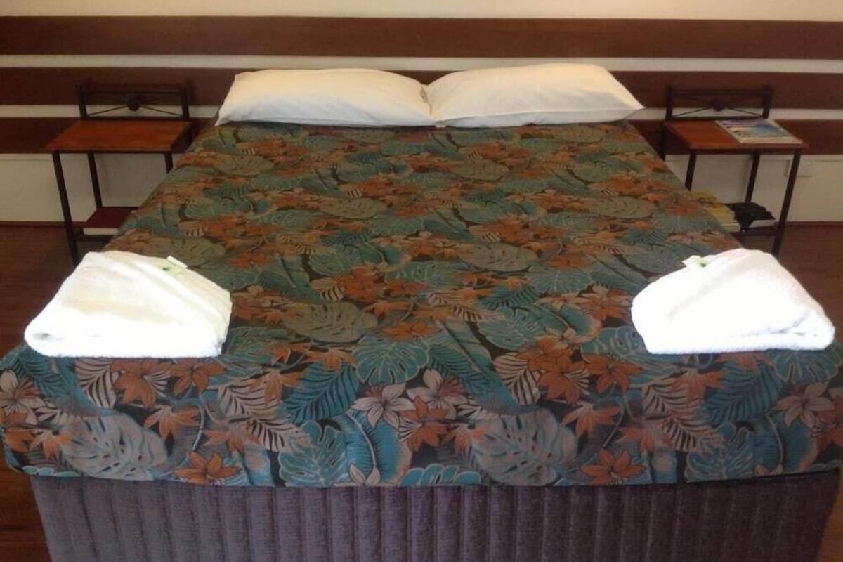 A bed with a floral bedspread, two pillows, and two towels on the bed.
