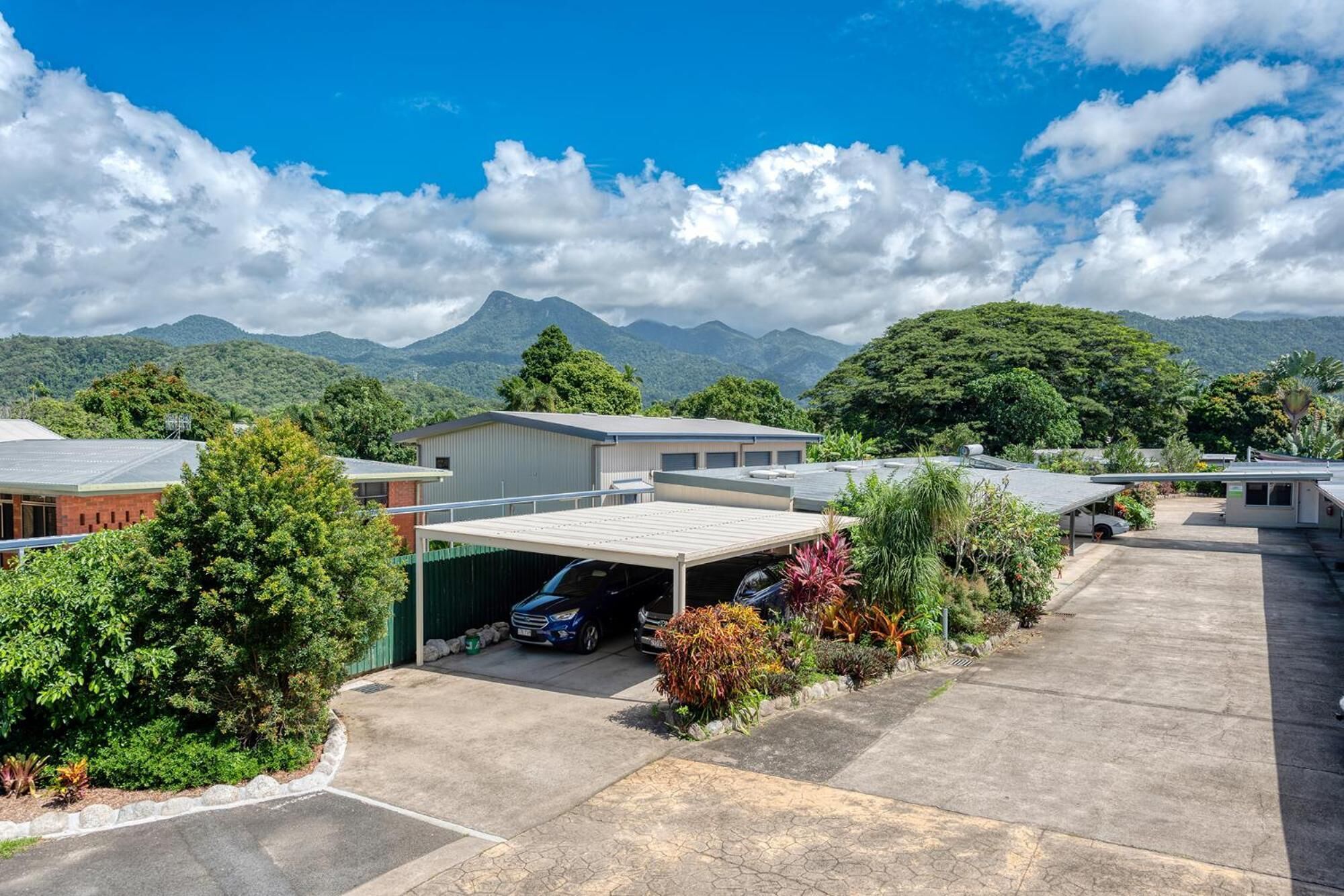 Uma área de estacionamento com uma garagem coberta, rodeada por vegetação e edifícios com telhados planos.