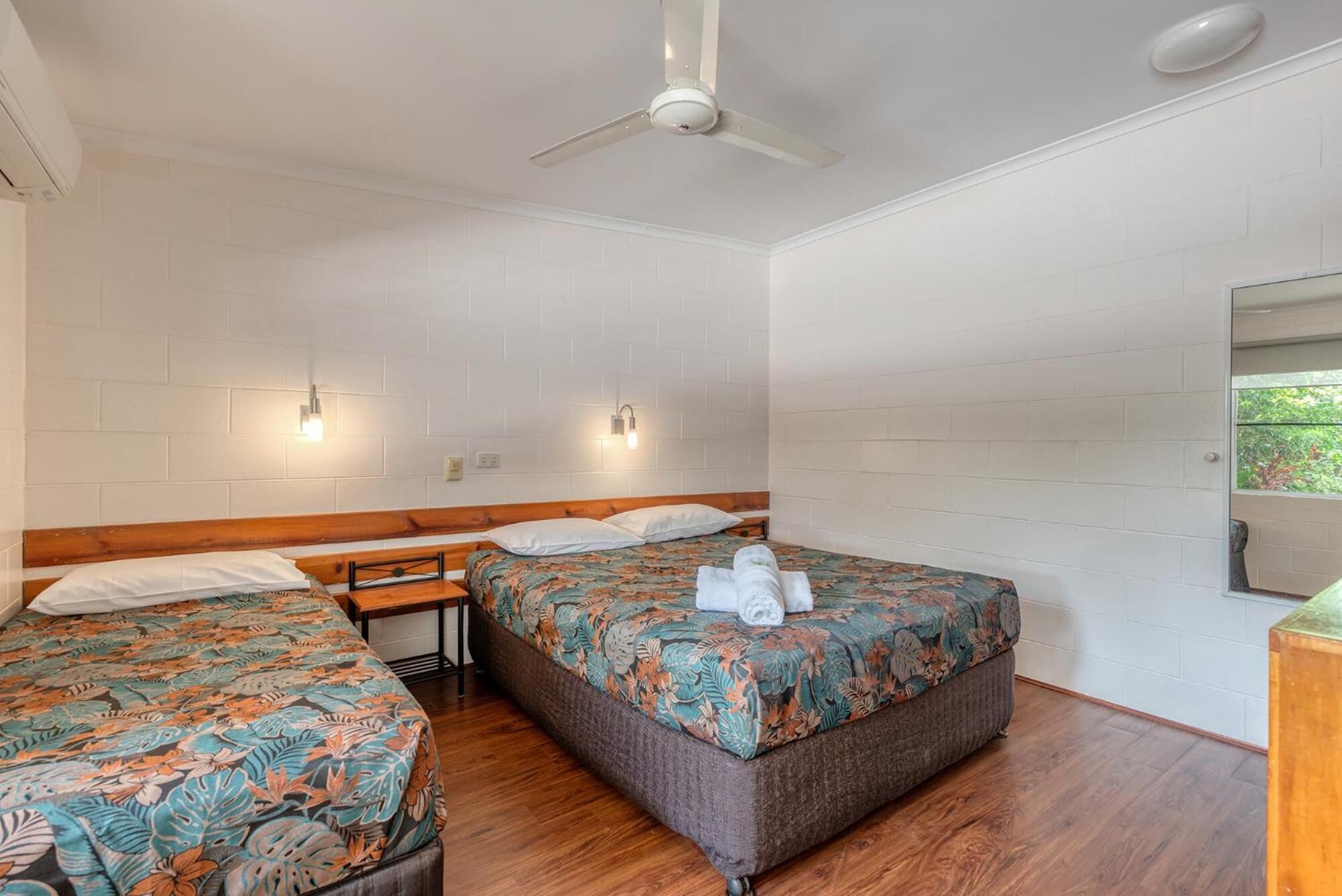 A room with two beds, a ceiling fan, and a wooden bench.