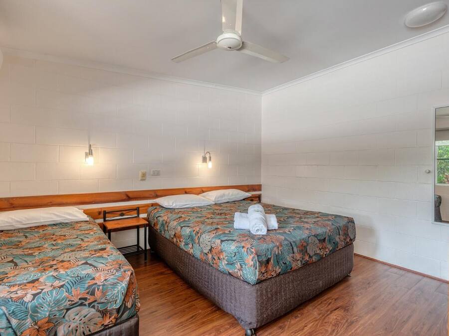 A room with two beds, a ceiling fan, and a wooden bench.