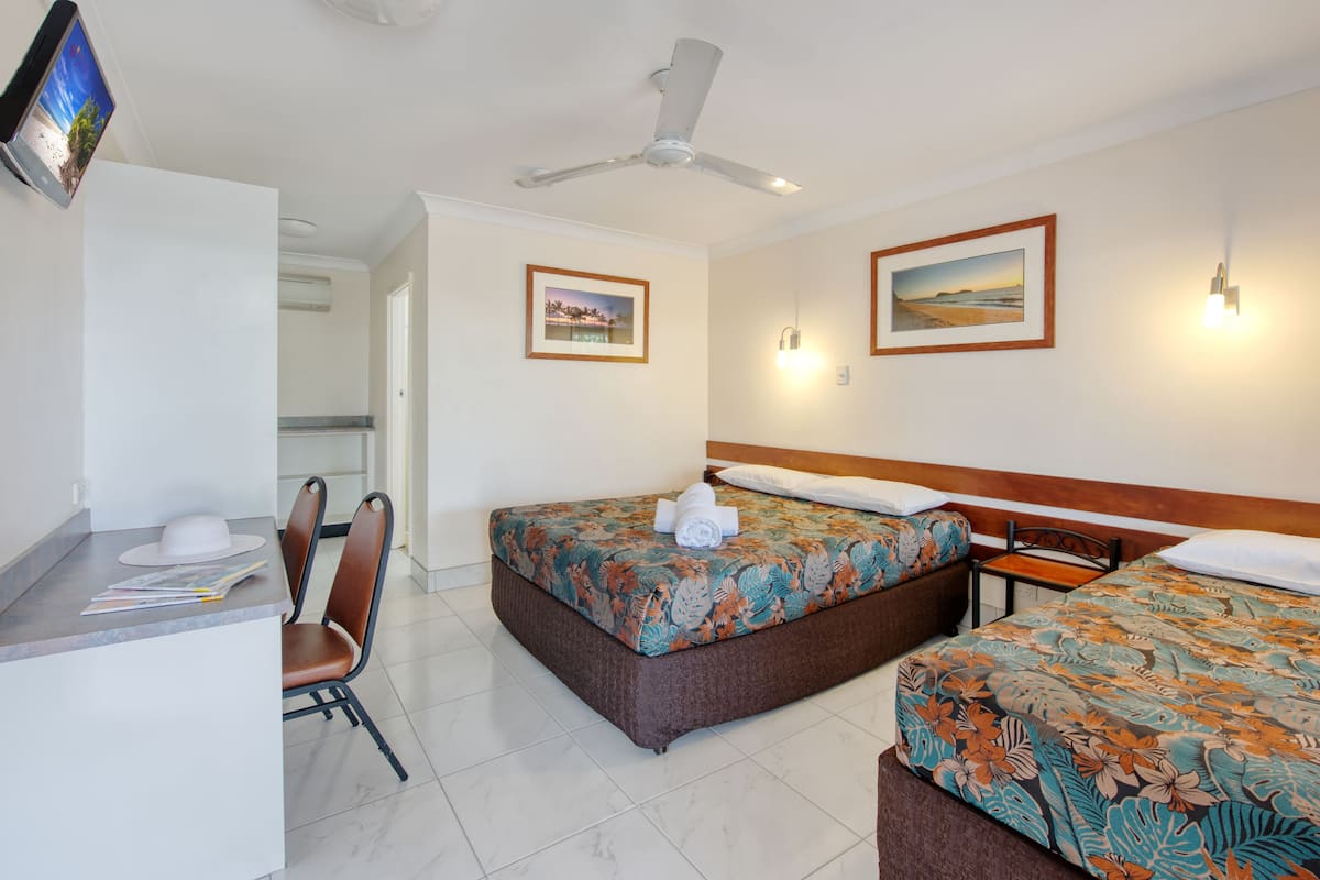 A hotel room with two beds, a desk, a chair, and a ceiling fan.
