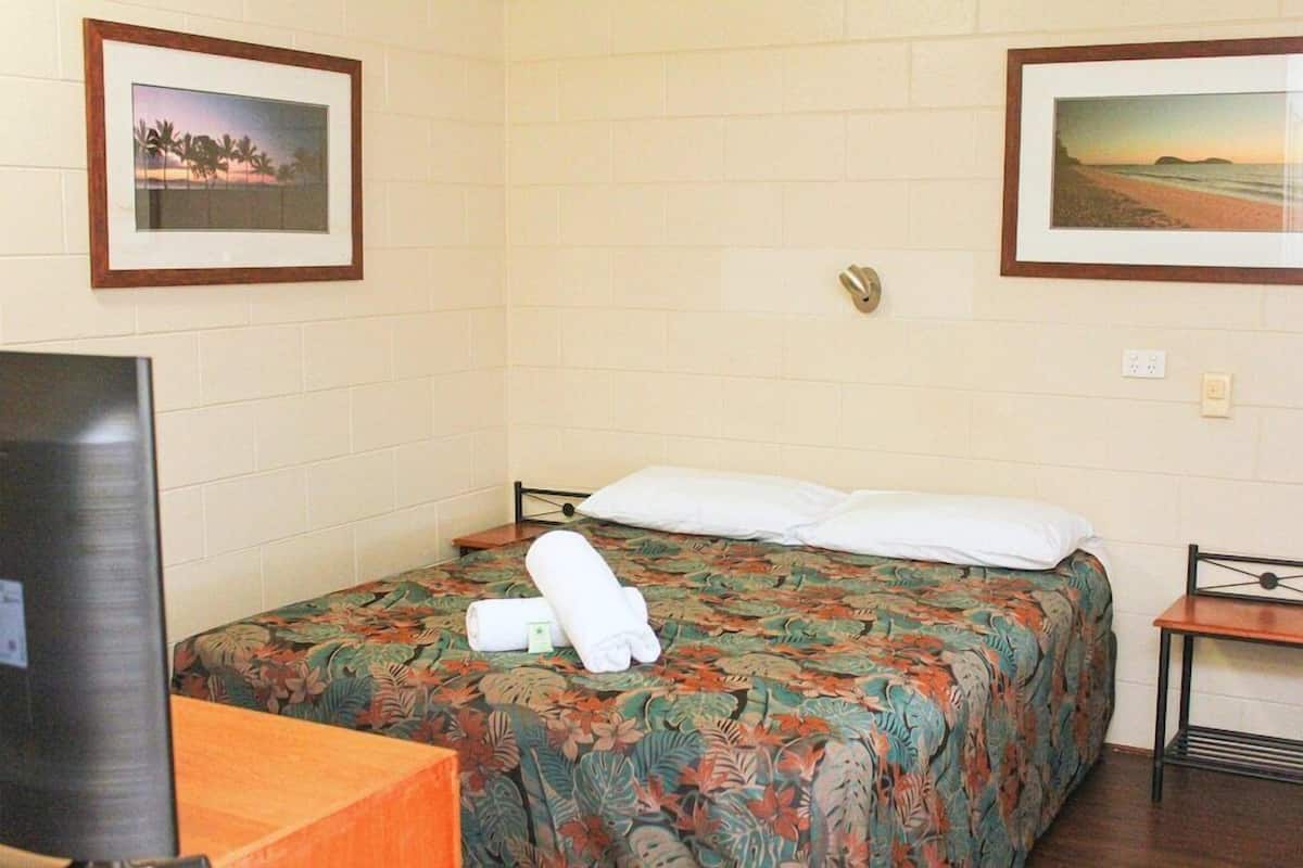 A hotel room with a bed, a television, and two framed pictures on the wall.