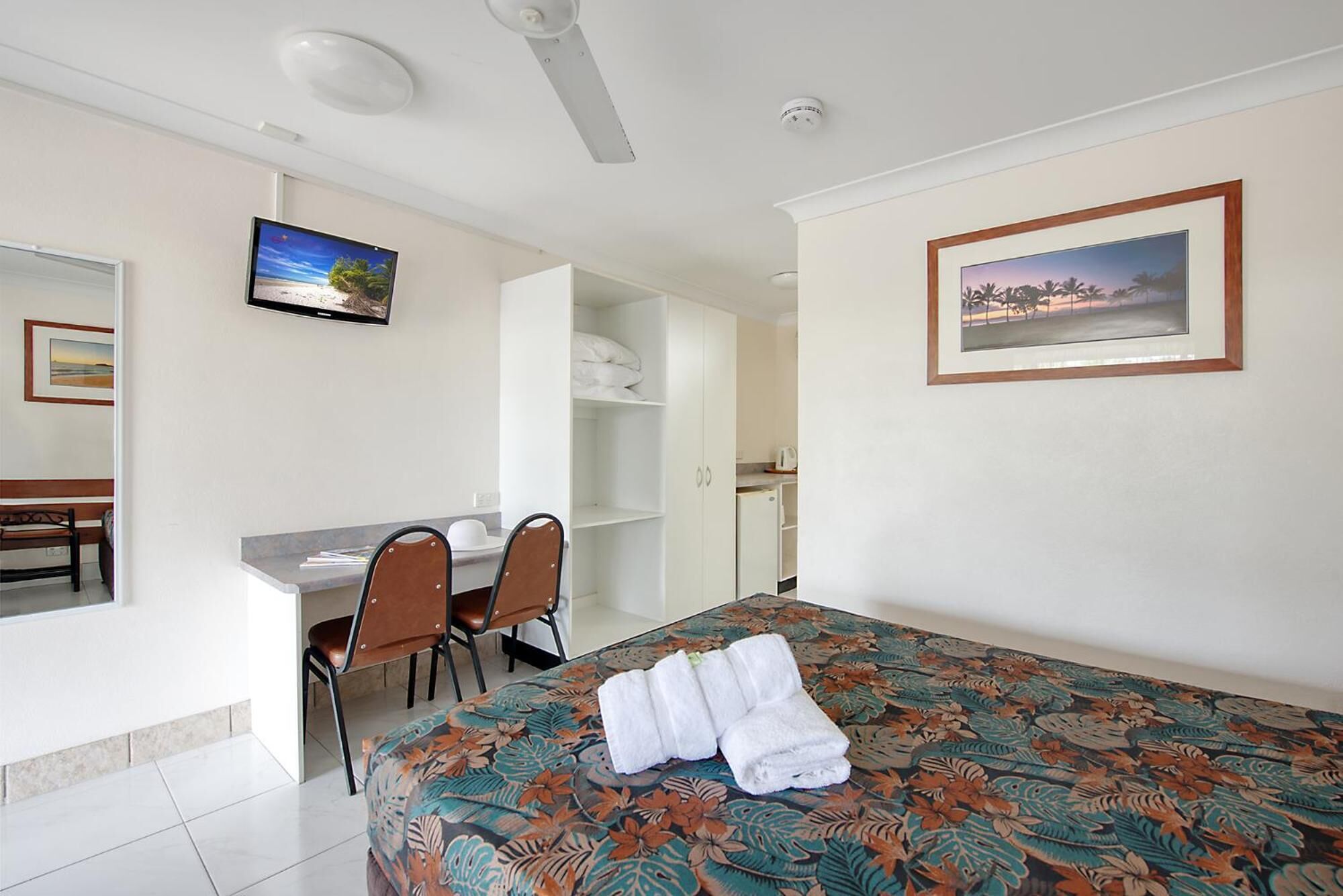 A hotel room with a bed, a desk, two chairs, a wardrobe, and a bathroom visible through an open door.