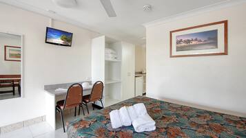 A hotel room with a bed, a desk, two chairs, a wardrobe, and a bathroom visible through an open door.