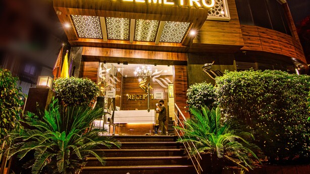 A modern hotel entrance with a sign reading "LAHOTELMETRO," featuring a staircase, potted plants, and a well-lit facade. - LA Hotel Metro (Mumbai)