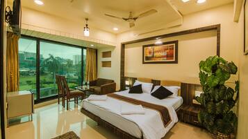 A hotel room with a large bed, a desk, a chair, a large window with a view, and a ceiling fan.