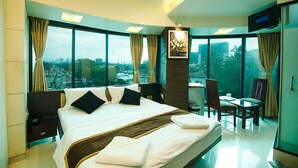 A modern hotel room with a large bed, a desk, and a chair. There is a TV mounted on the wall and a window with a city view. - LA Hotel Metro (Mumbai)