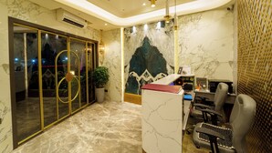A reception area with marble flooring, a reception desk, two chairs, a potted plant, and a decorative wall mural. - LA Hotel Metro (Mumbai)