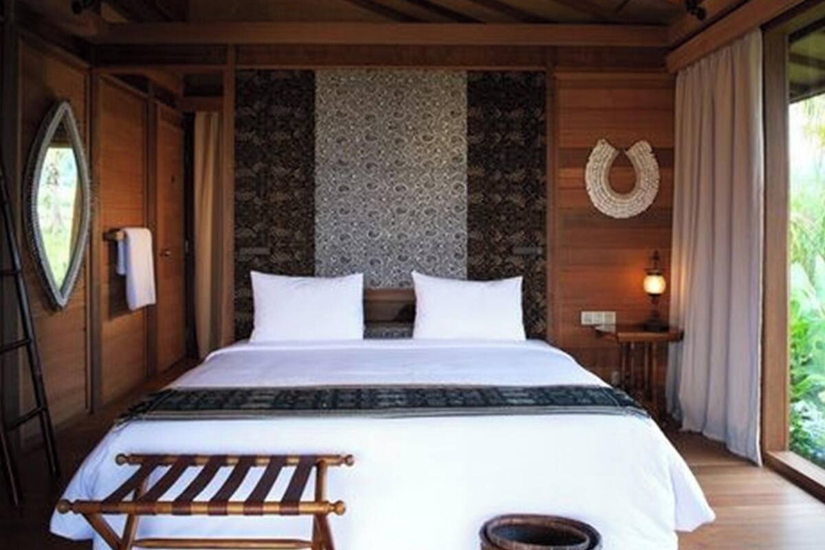 A wooden room with a bed, a ladder, a wall-mounted mirror, and a patterned wall.