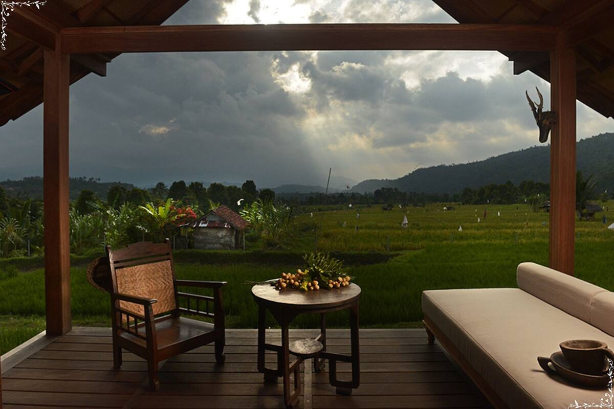 A wooden deck with a sofa and a chair, overlooking a green landscape with a hill in the distance.