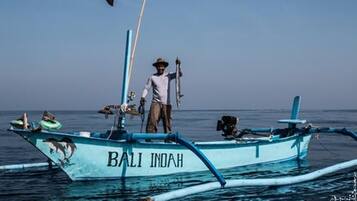 Ein Boot namens "BALI INDAH", auf dem eine Person mit einem Fischernetz steht.